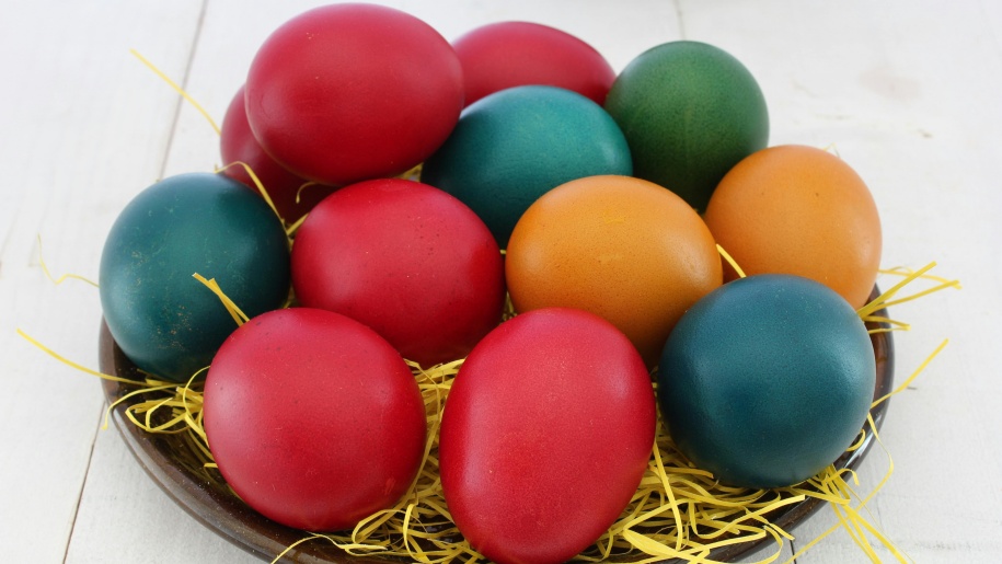 Twelve brightly coloured eggs in a dish.