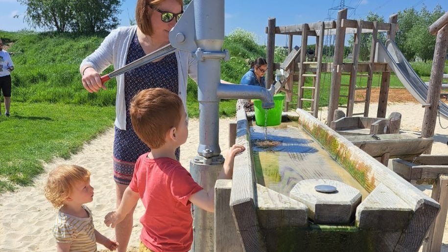 A family using the water pump to fill a bucket in the playground at Hogshaw Farm & Wildlife Park.