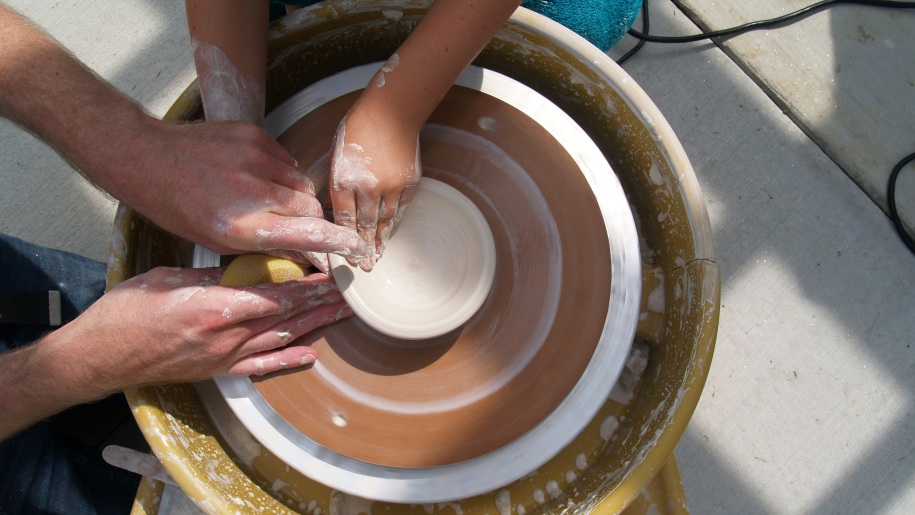 An adult helping a child to throw on the potter's wheel.