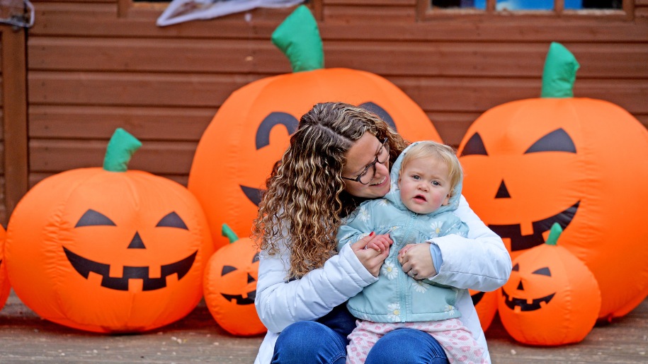 An adult holding a baby in front of orange pumpkins at Conkers.