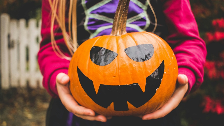 A child's hands holding a pumpkin decorated for Halloween.