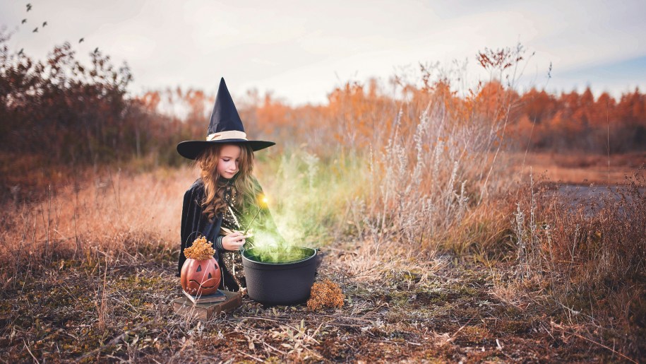 Girl dressed in witch's costume sitting by a cauldron.