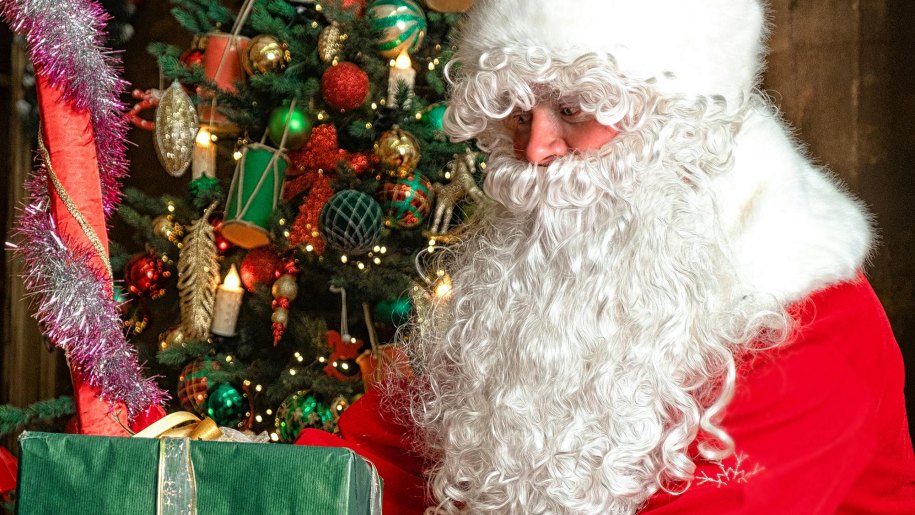 Santa holding a present by a Christmas tree.