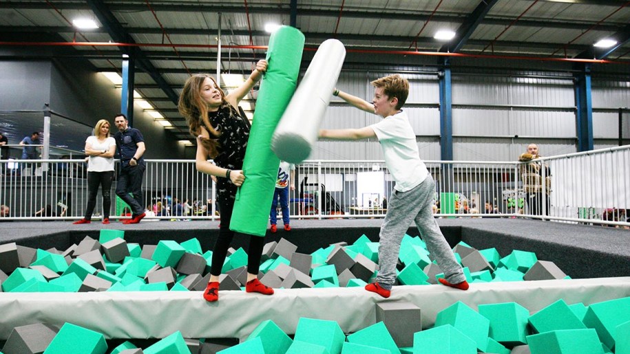 Children battling it out on a balance beam over a foam pit.