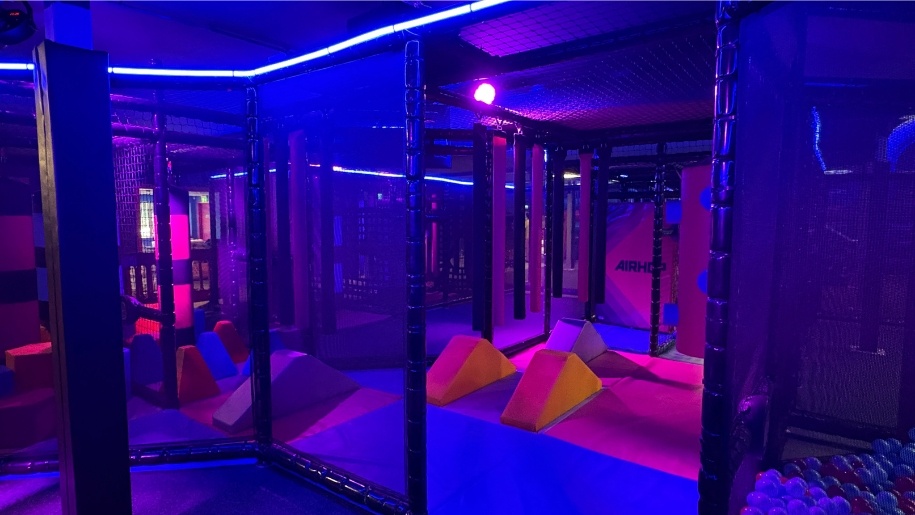 Trampoline attractions at AirHop Gloucester illuminated by pink and purple lighting.