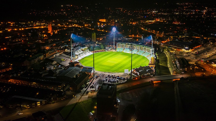 Aerial view of a floodlit grassed sports arena surrounded by stands.