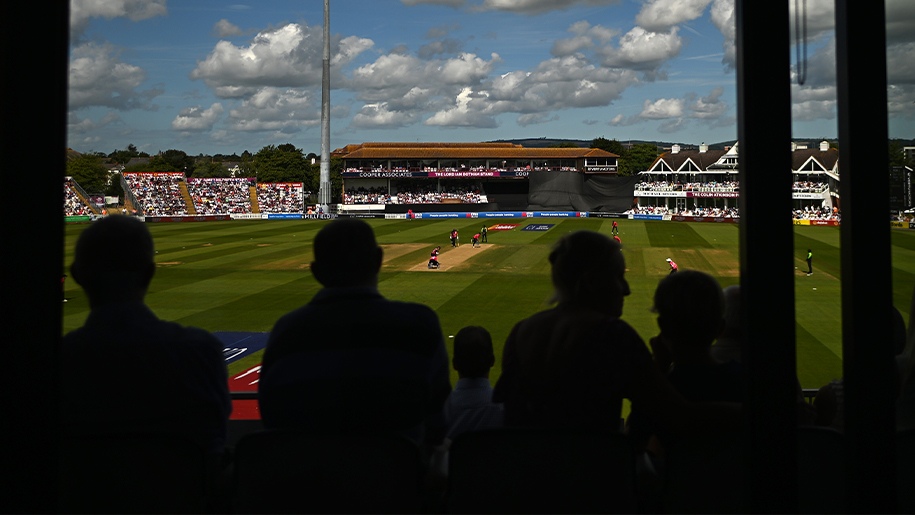 A cricket match with spectators in the stands in the foreground.