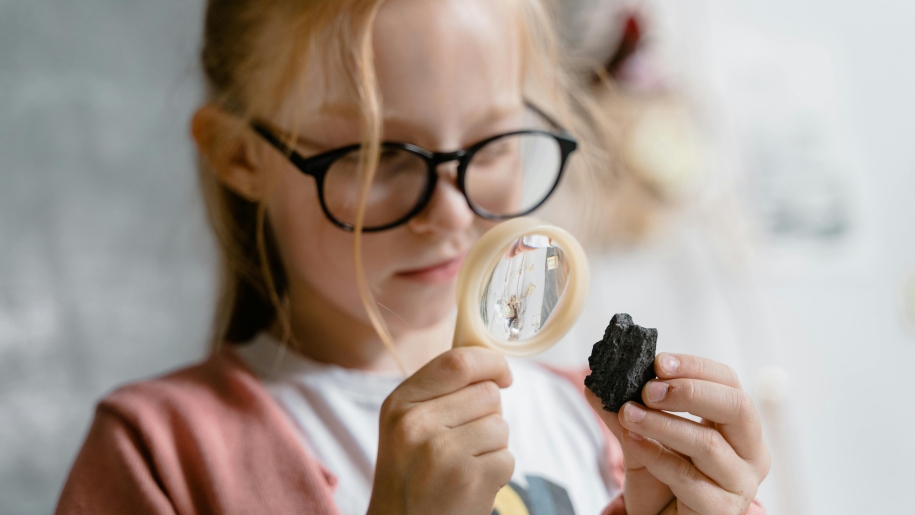 A girl looking at a rock through a magnifying glass.