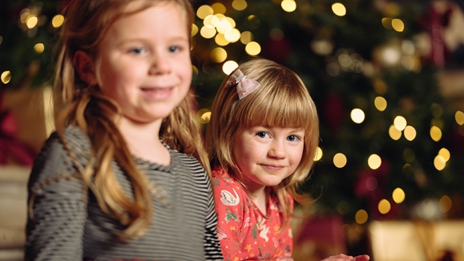 Two little girls sitting by a twinkling Christmas tree.