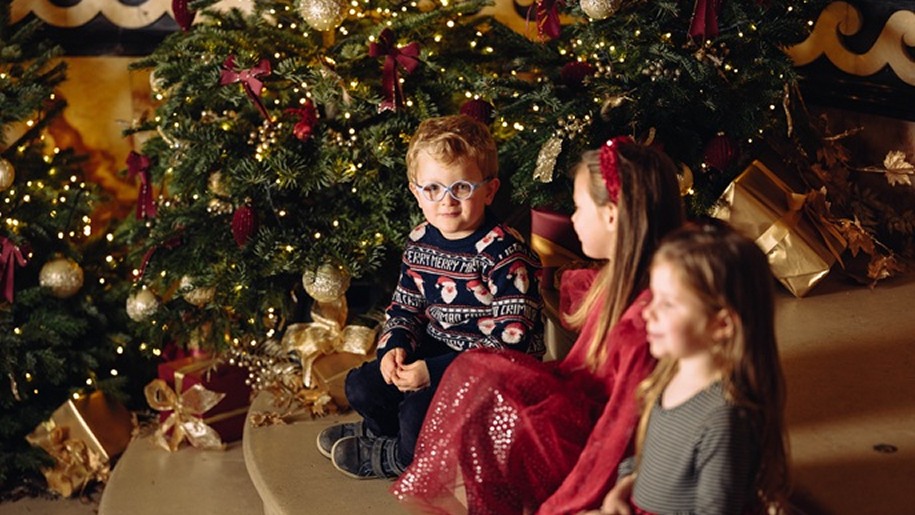 Three children sitting around a Christmas tree.