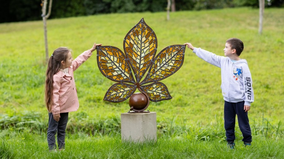 Two children standing by a sculpture of a flower.