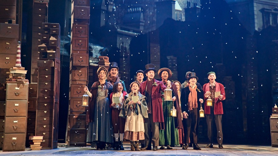 A group of actors in Victorian costume on stage.