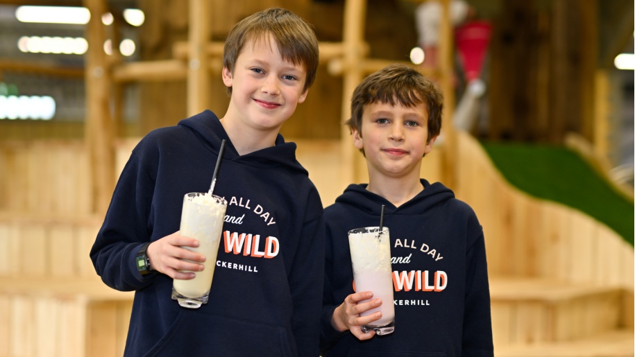 Two boys holding highball glasses containing straws and white drinks.