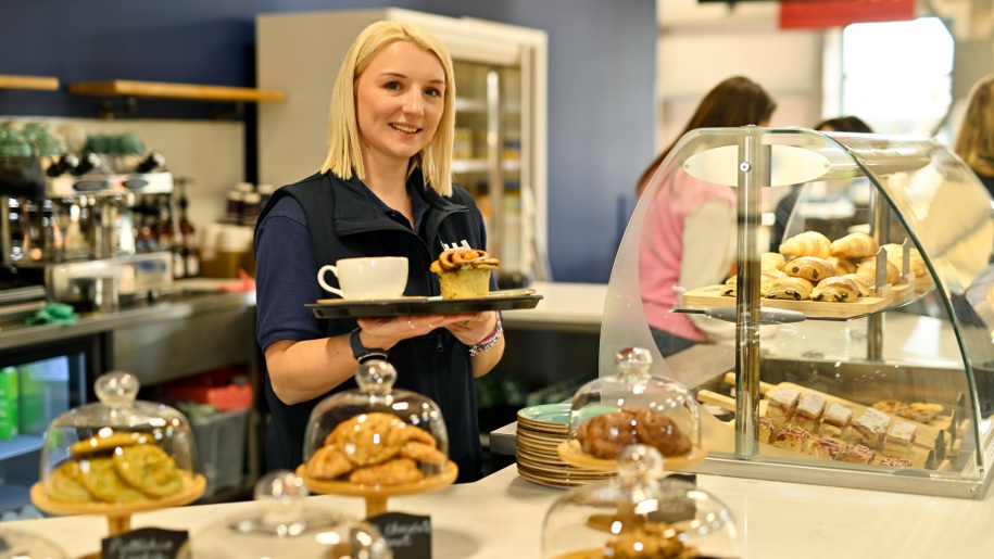 Woman holding a tray with coffee and cake in a cafe.