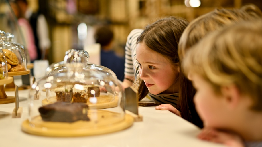 Children looking at cakes under glass domes in a cafe.