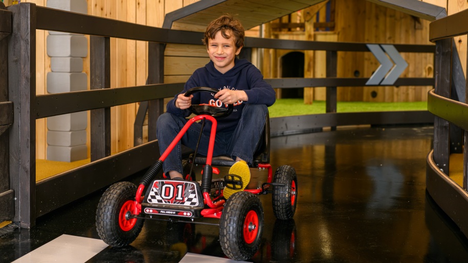 Boy driving a go kart around an indoor track.