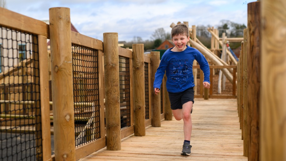 Boy running over a wooden bridge.