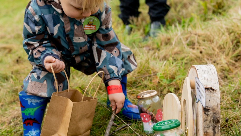 Young child picking a stick up on an autumn scavenger hunt.