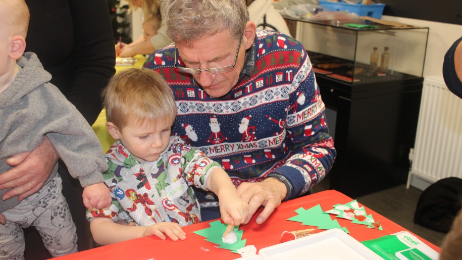Man helping a young child make a Christmas decoration.