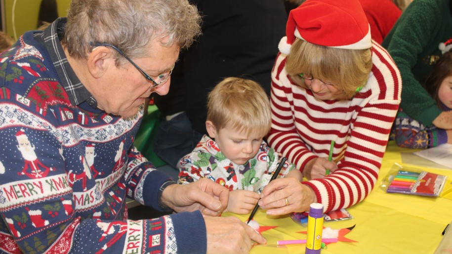 Adults helping a young child make a Christmas decoration.