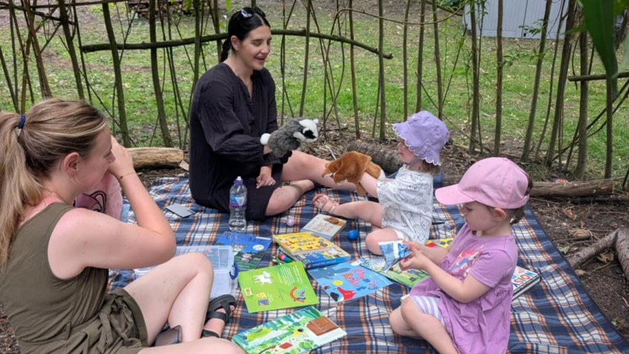 Adults and young children playing with glove puppets on a rug in a garden.