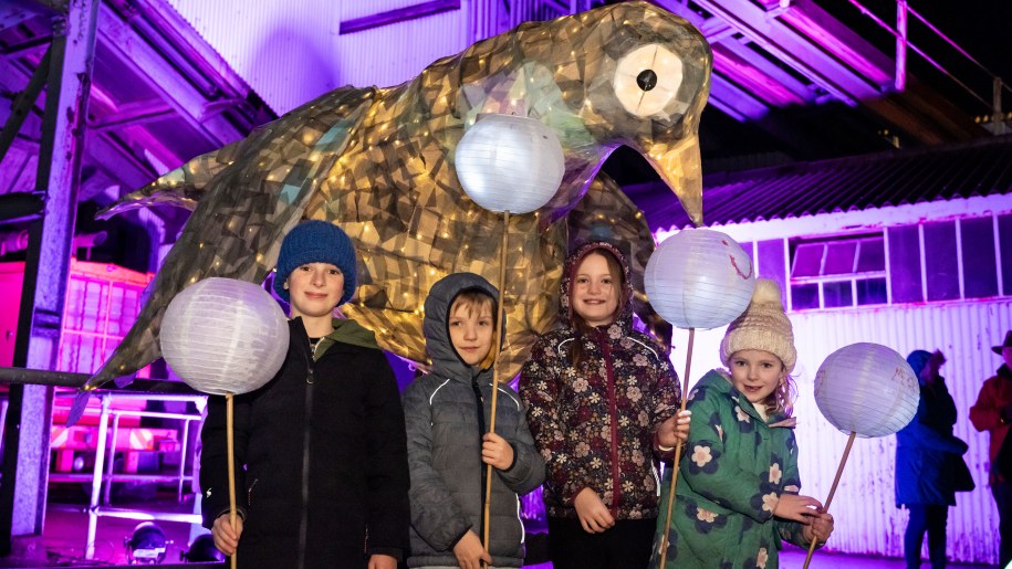 Children with paper lanterns in front of a huge lantern in shape of a bird..