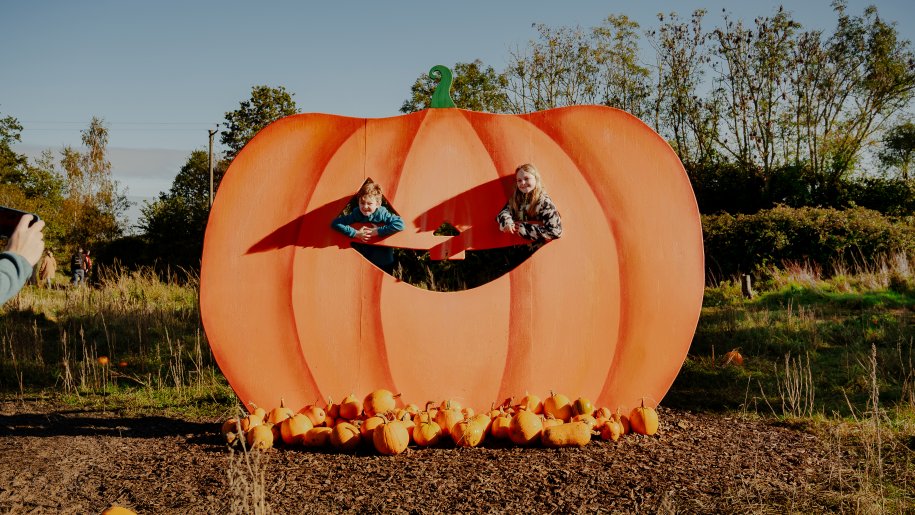Two children looking through a huge orange pumpkin cut-out.