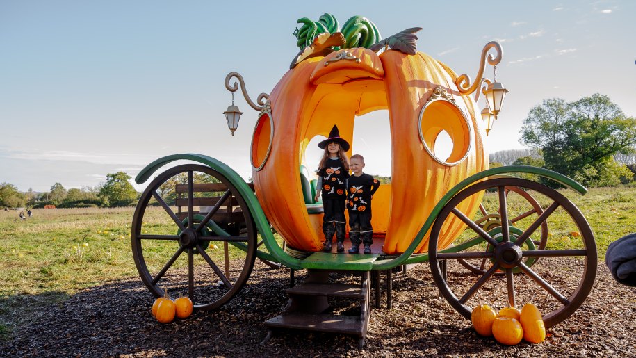 Two children in Halloween fancy dress in a huge pumpkin carriage.