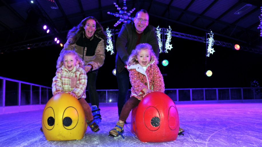 Parents with two small children using skate aids on a skating rink.