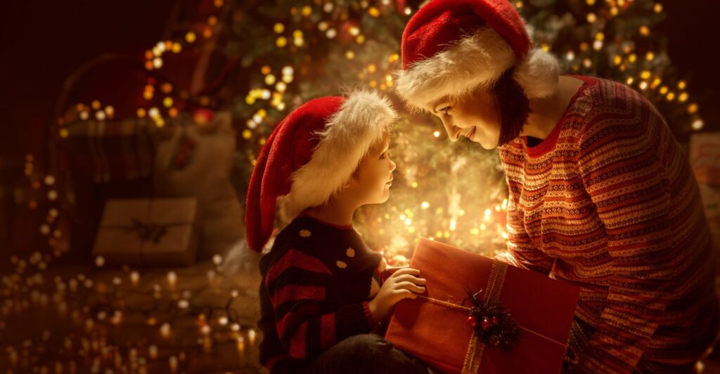 Family open Christmas Lighting Present Gift Box front of Xmas Tree, Happy Mother with Baby Child in Magic