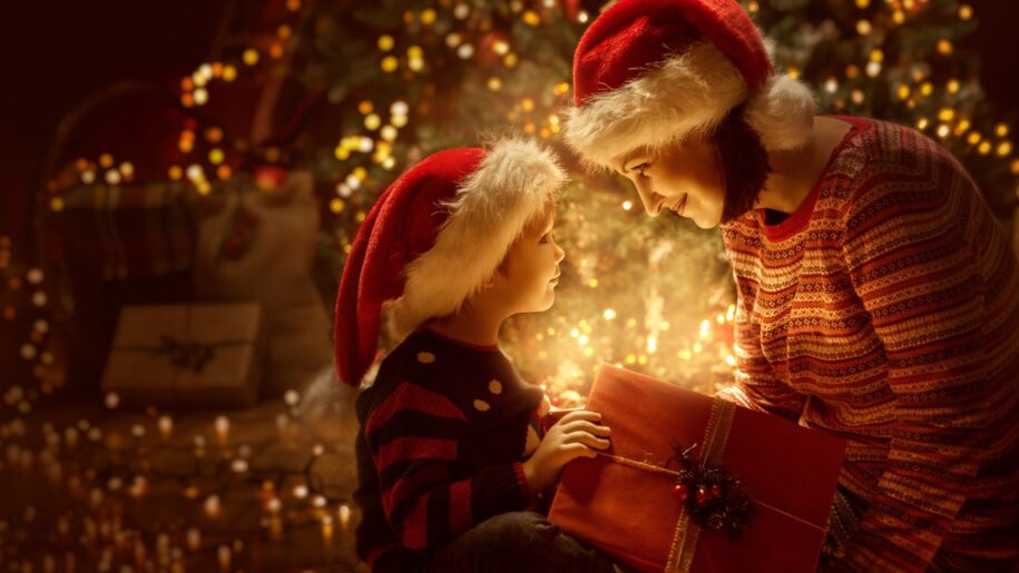 Family open Christmas Lighting Present Gift Box front of Xmas Tree, Happy Mother with Baby Child in Magic