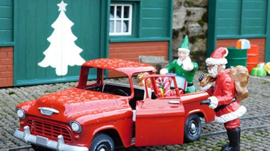 Model Santa and elves by a little red car in a festive scene.