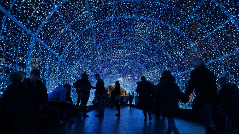 People walking through a tunnel of blue lights after dark.