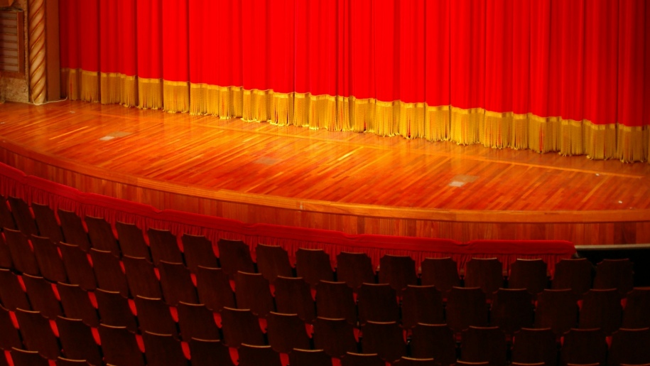 Red curtains with golden edging drawn across a theatre stage.