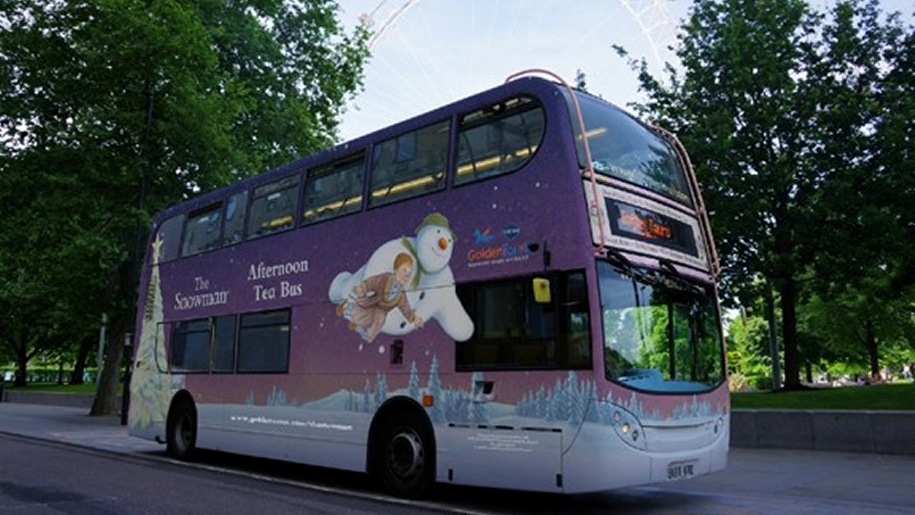 Purple double-decker bus with a picture of a flying snowman carrying a small boy on the side of it.