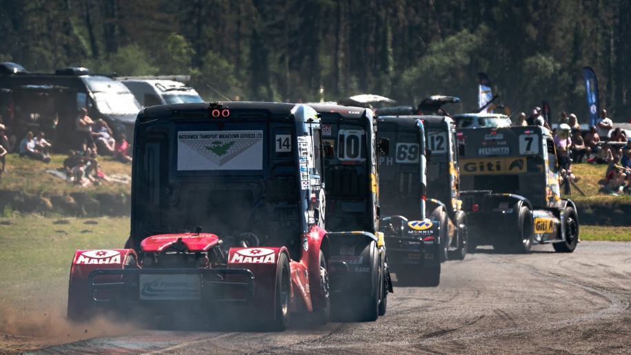 Convoy of black trucks at a race circuit.