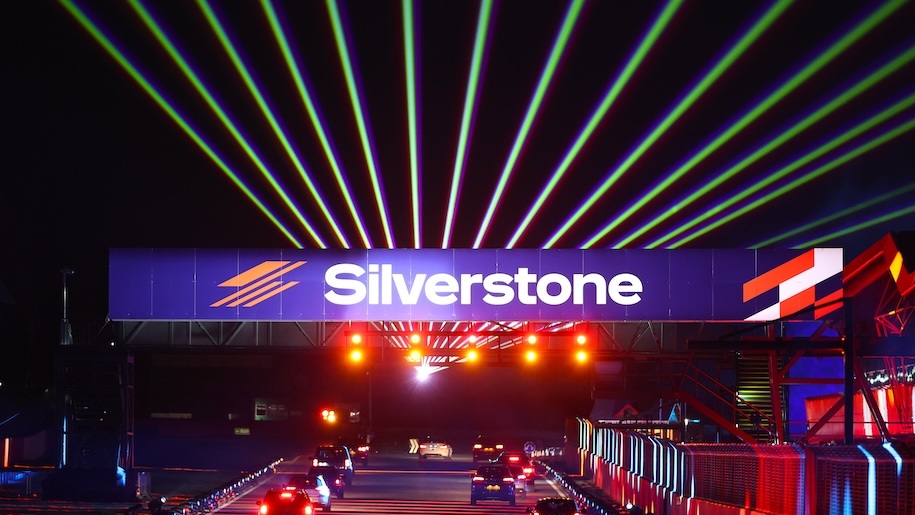 Cars driving around Silverstone Circuit illuminated by Christmas lights.