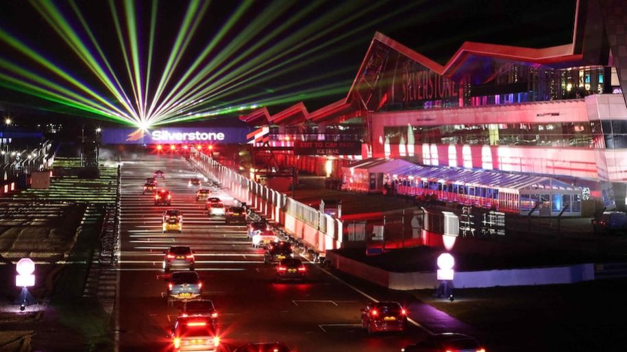 race circuit at night with line of cars, stands and lights