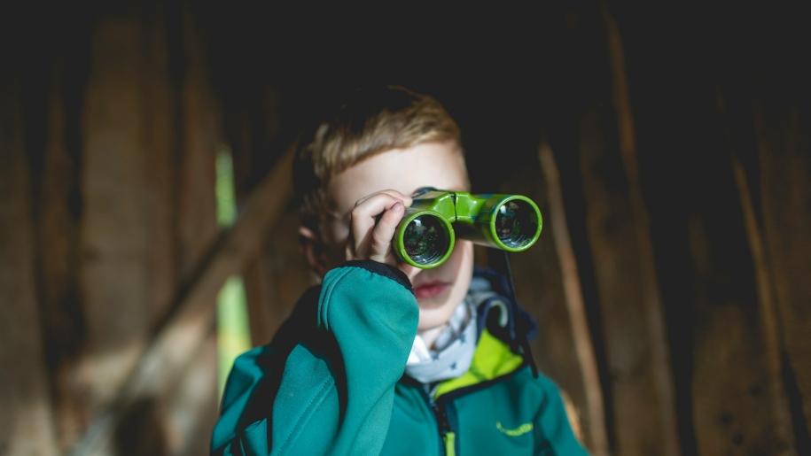 Boy in a turquoise jacket using a pair of green binoculars.