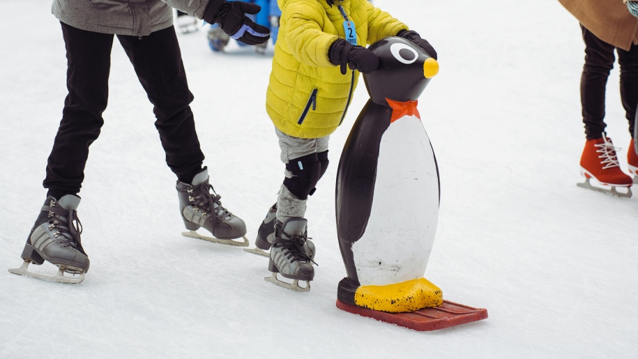 Child using a penguin skate aid at an ice rink.