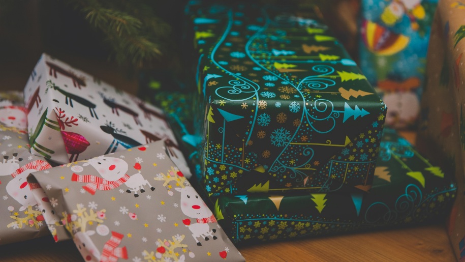 A pile of colourfully wrapped Christmas presents under a tree.