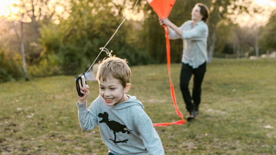 Father and son flying an orange kite in green space.