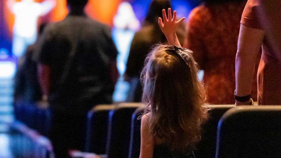 Child waving in the audience at a theatre show.