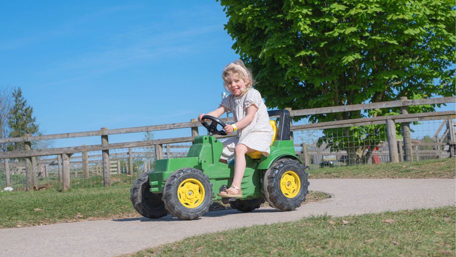 girl on toy tractor with blue sky behind
