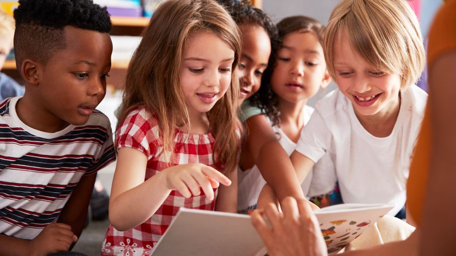 mix of children looking at a book shown by a teacher