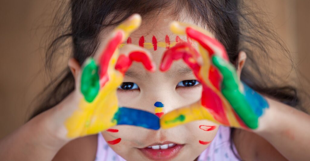 girl with paint on hands makes a heart shape to camera