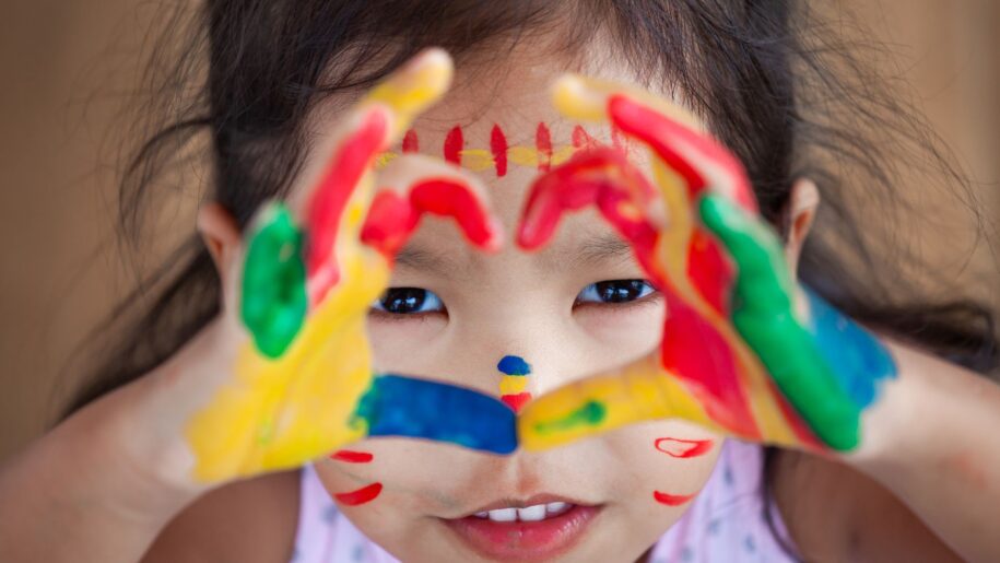 girl with paint on hands makes a heart shape to camera