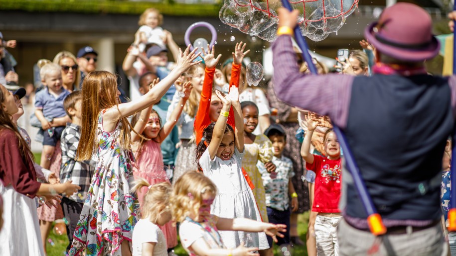A crowd of children reaching up to catch bubbles on a sunny day.