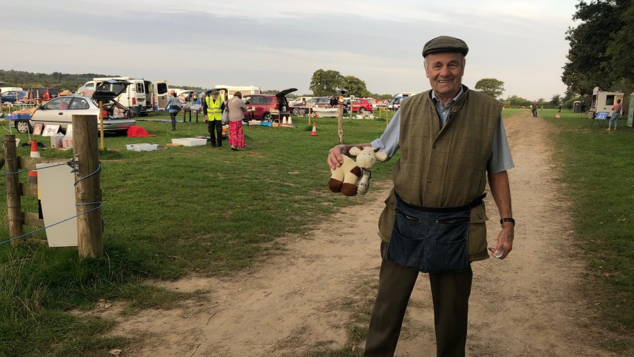 Man holding a small cow soft toy with a car boot sale in the background.