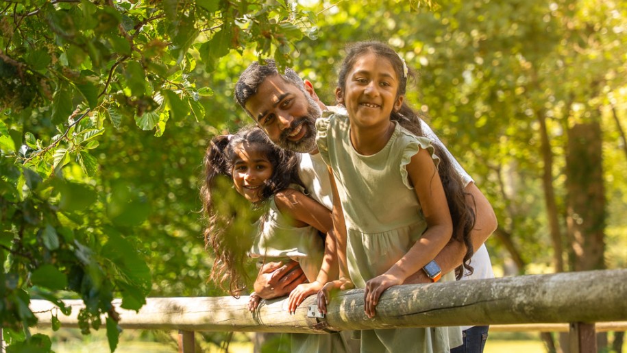 Father and his two children leaning over wooden railings to look at something.